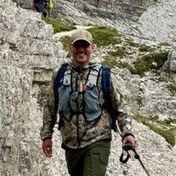 Scott Neve, hiking pack on, grinning on a mountain path in the Dolomites.
